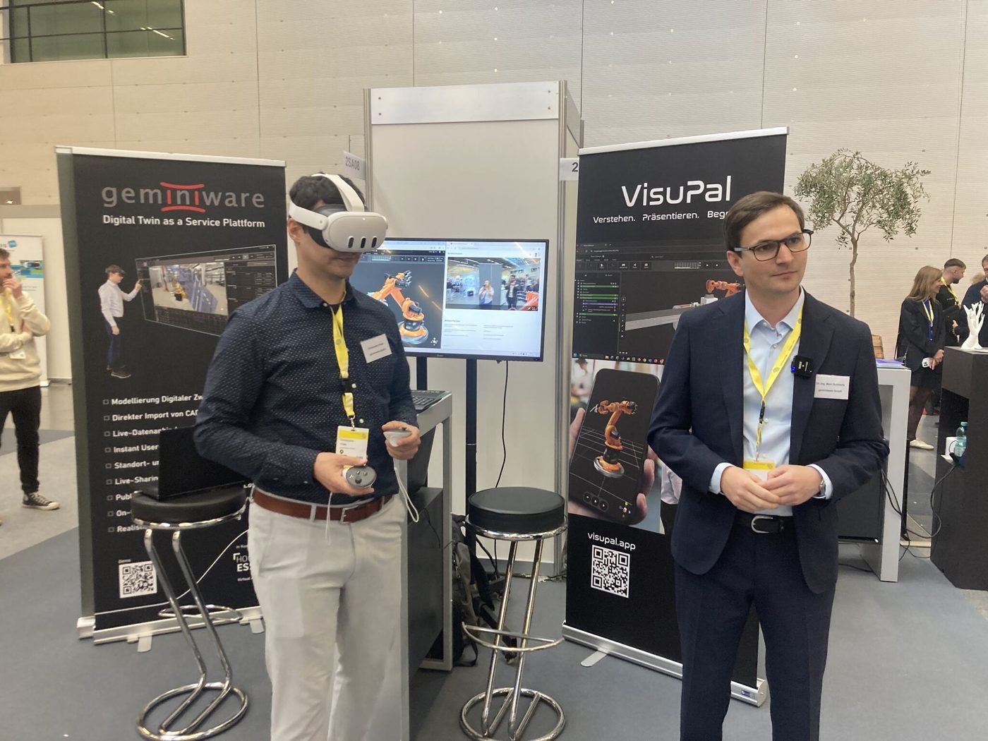 Teammitglieder am Messestand mit VR-Brille und Digitalem Zwilling auf dem Bildschirm